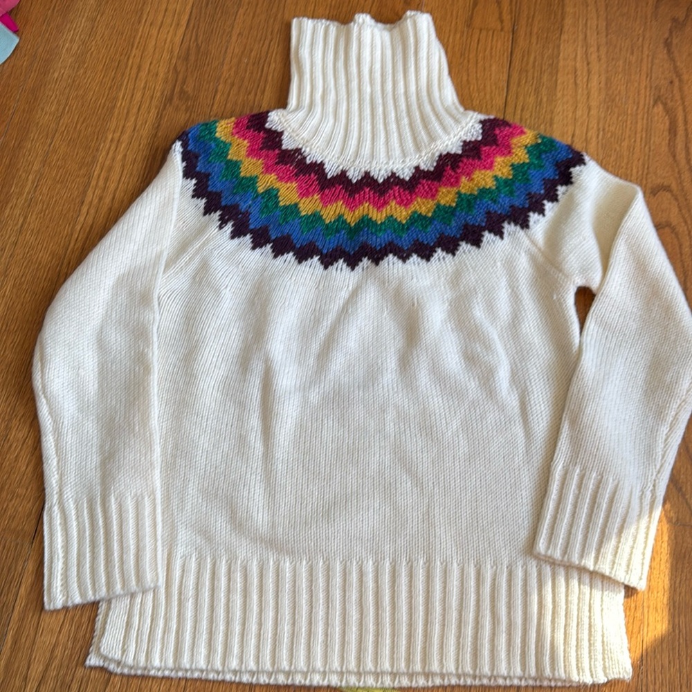 Cream turtleneck tunic sweater with multicolor ring at top.